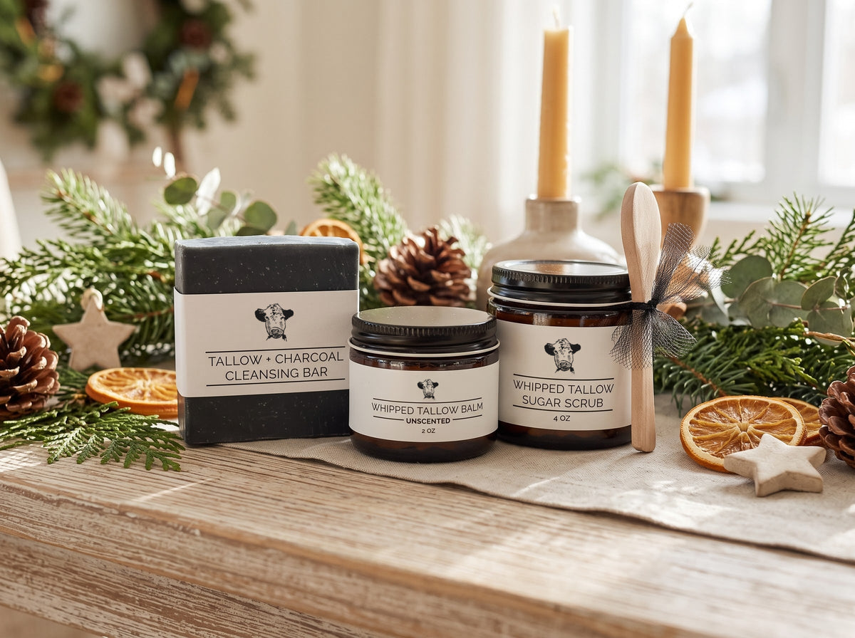 Complete Tallow Routine Set: Tallow + Charcoal Cleansing Bar, 2 oz Unscented Whipped Tallow Balm, and 4 oz Whipped Tallow Sugar Scrub with a wooden spoon on a wooden table with pine, dried oranges, pinecones, and beeswax candles